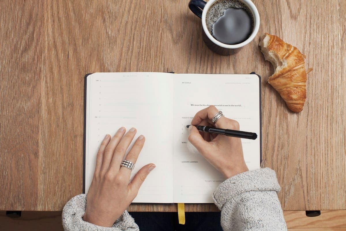 Someone writing in a journal beside a cup of coffee